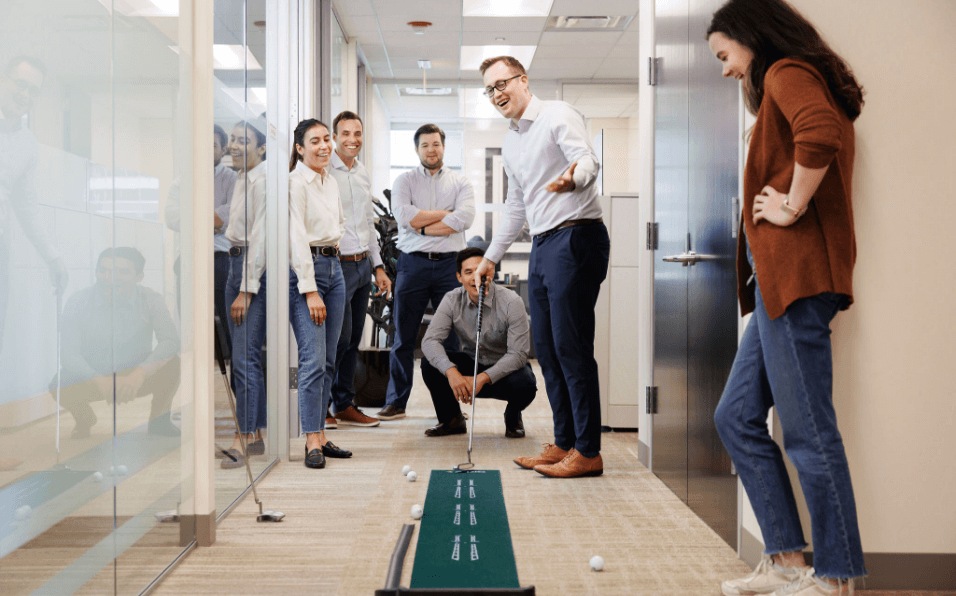 Team playing on putting grass in office hallway