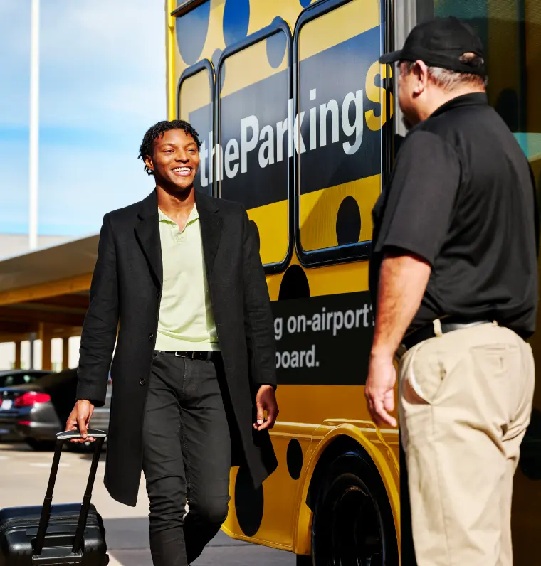 The parking spot hero image, a man is walking towards the driver of the parking spot bus with his luggage smiling